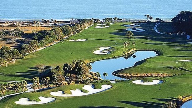 A golf course with water hazards, sand bunkers, and a view of the ocean.