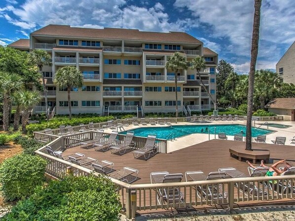 A hotel with a pool area, multiple balconies, and lush greenery.