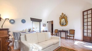 Un salon comprenant un canapé, des fauteuils, une table avec un vase et une porte à panneaux de verre.