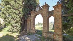 Une arche en pierre au style rustique et d’époque, entourée de verdure et d’arbres.