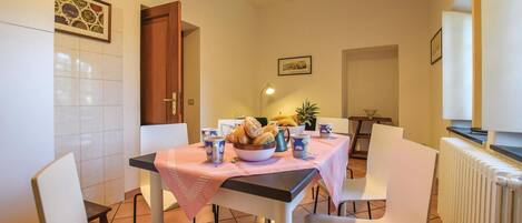 A dining area with a table set for four, a bowl of bread, a pineapple, and a coffee pot.