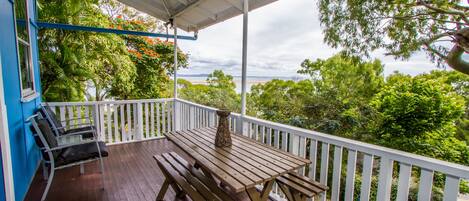A wooden deck with a table and benches, surrounded by white railings and lush greenery.