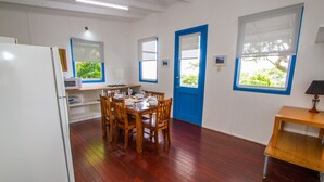 A compact kitchen with a dining area, wooden flooring, and a blue door. - Sunset Villa • Pet-Friendly Studio with Ocean Views in Beautiful 1770 (1770)