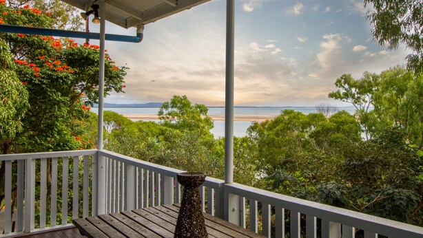 A wooden deck with a railing, overlooking a beach and ocean with trees and flowers in the foreground. - Sunset Villa • Pet-Friendly Studio with Ocean Views in Beautiful 1770 (1770)