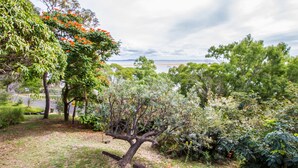 A lush garden with various trees and shrubs, a grassy area, and a view of a body of water in the distance. - Sunset Villa • Pet-Friendly Studio with Ocean Views in Beautiful 1770 (1770)