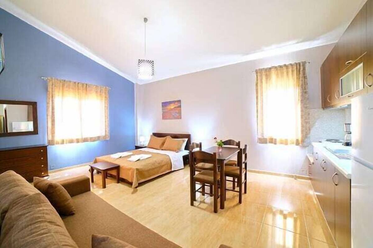 A hotel room with a bed, a dining table, a sofa, a kitchen area, and a painting on the wall.