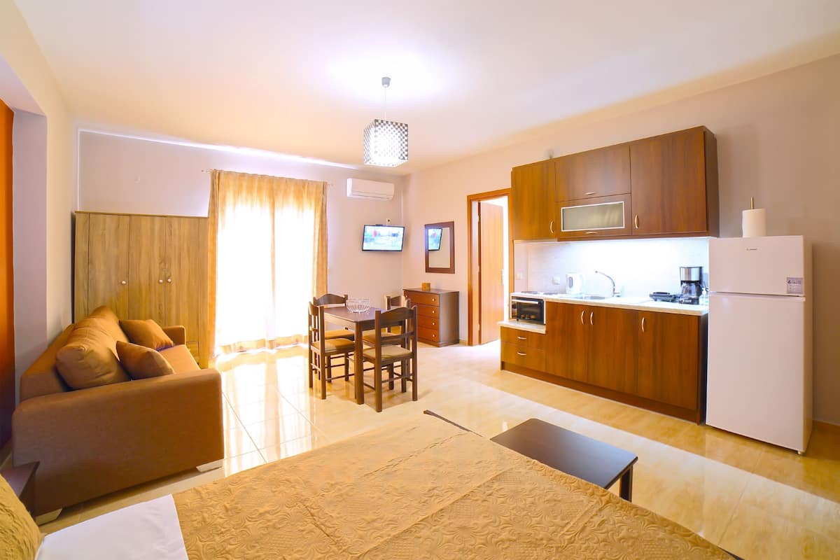 A compact living space with a sofa, dining table, chairs, a kitchen area with a microwave, stove, and refrigerator.