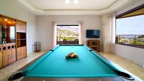 A pool table in a room with a view of a mountainous landscape through a large window. - Villas metoxi (Heraklion)
