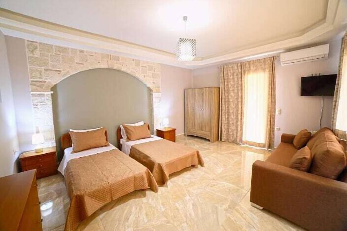 A hotel room with two beds, a sofa, a TV, and a stone wall.