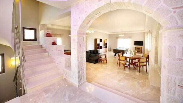 A spacious living area with a stone archway, a dining table, and a staircase leading to another level. - Villas metoxi (Heraklion)