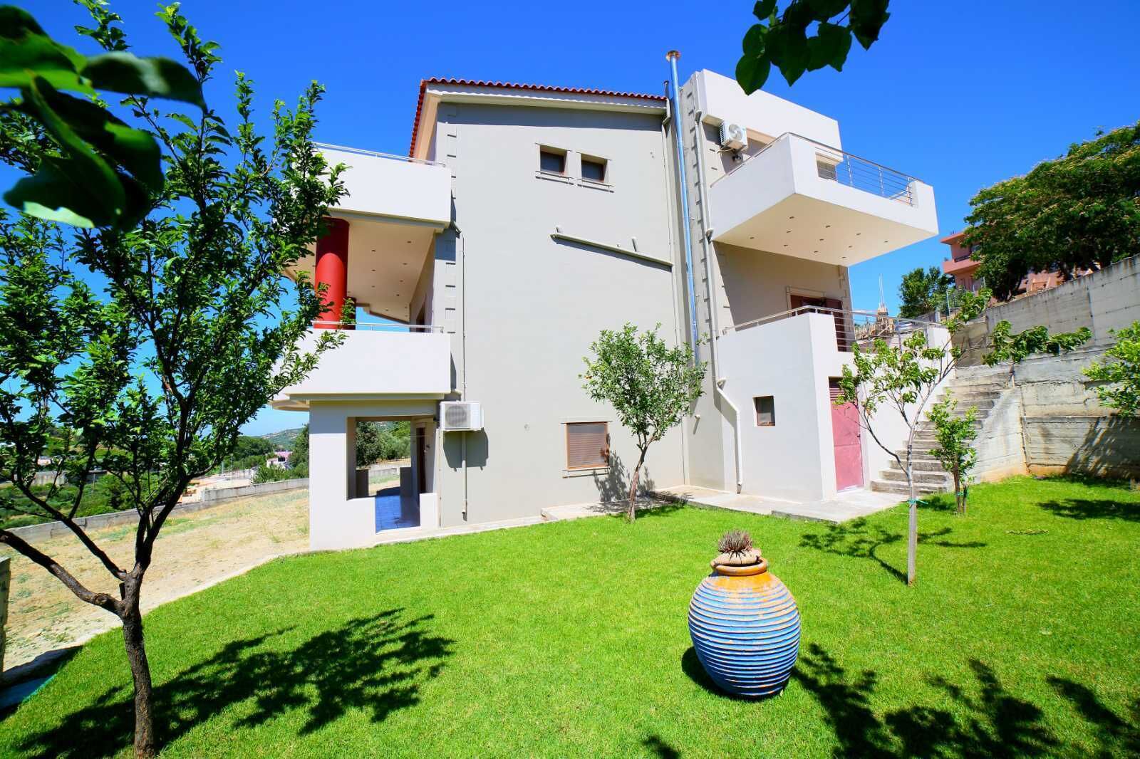 A modern two-story building with a flat roof, a small balcony on the upper floor, and a well-maintained lawn with a decorative vase.