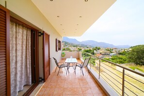 A balcony with a table and chairs, a view of a town and mountains, and a railing. - Villas metoxi (Heraklion)