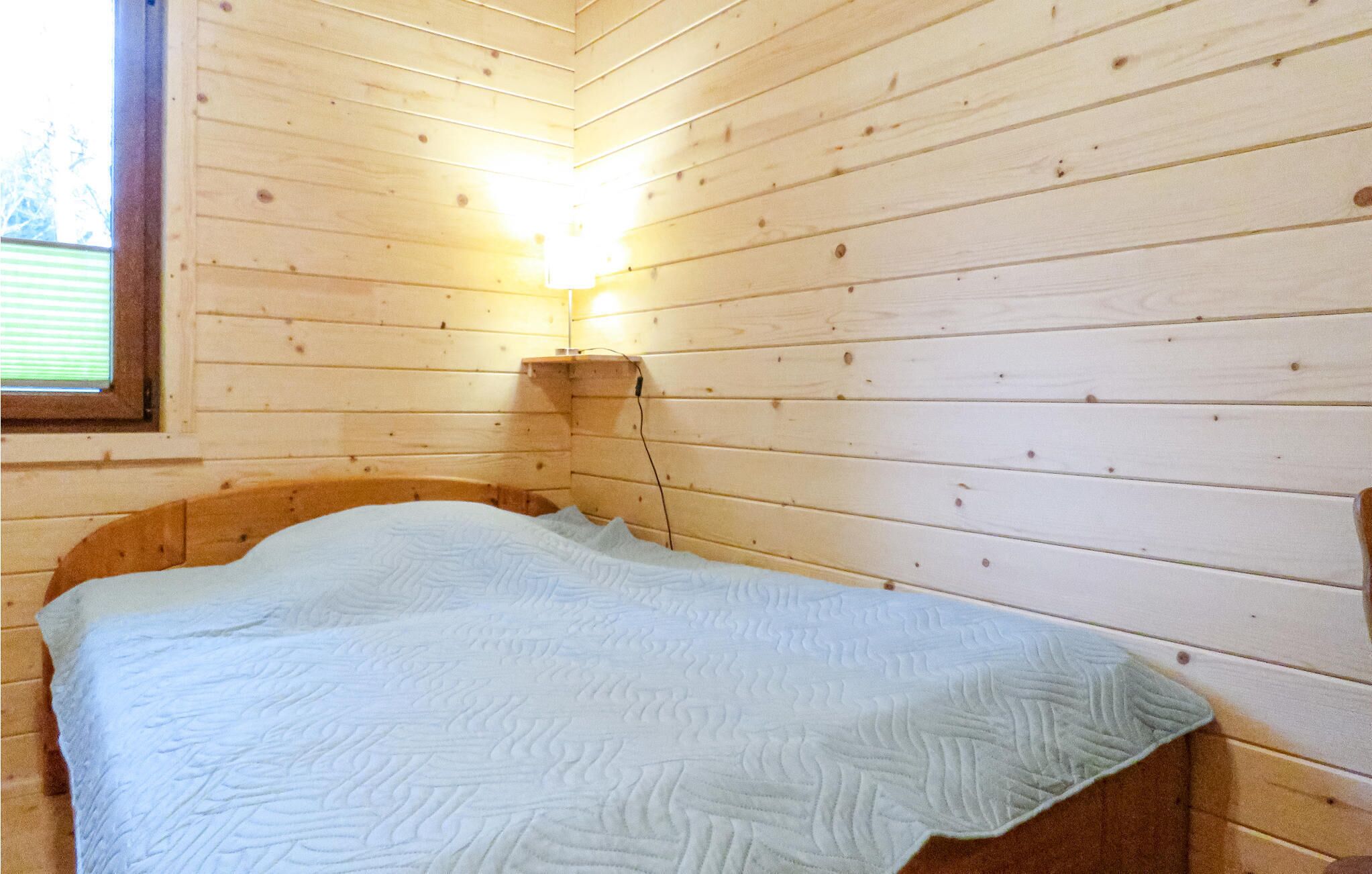 Et hyggeligt værelse i en træhytte med seng, et vindue og en lampe på væggen.