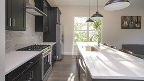 Een moderne keuken met donkere kastjes, een roestvrijstalen koelkast, een groot eiland met een spoelbak en hanglampen.