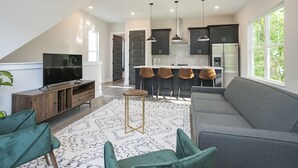 Een moderne keuken met donkere kastjes, een centraal eiland met barkrukken en een groot raam voor natuurlijk licht.