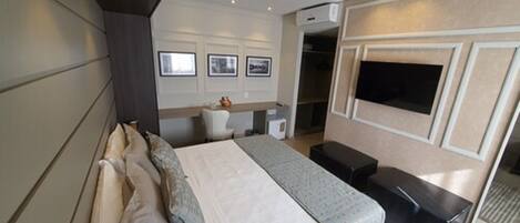 A modern hotel room with a large bed, a desk, a TV, and a wardrobe.