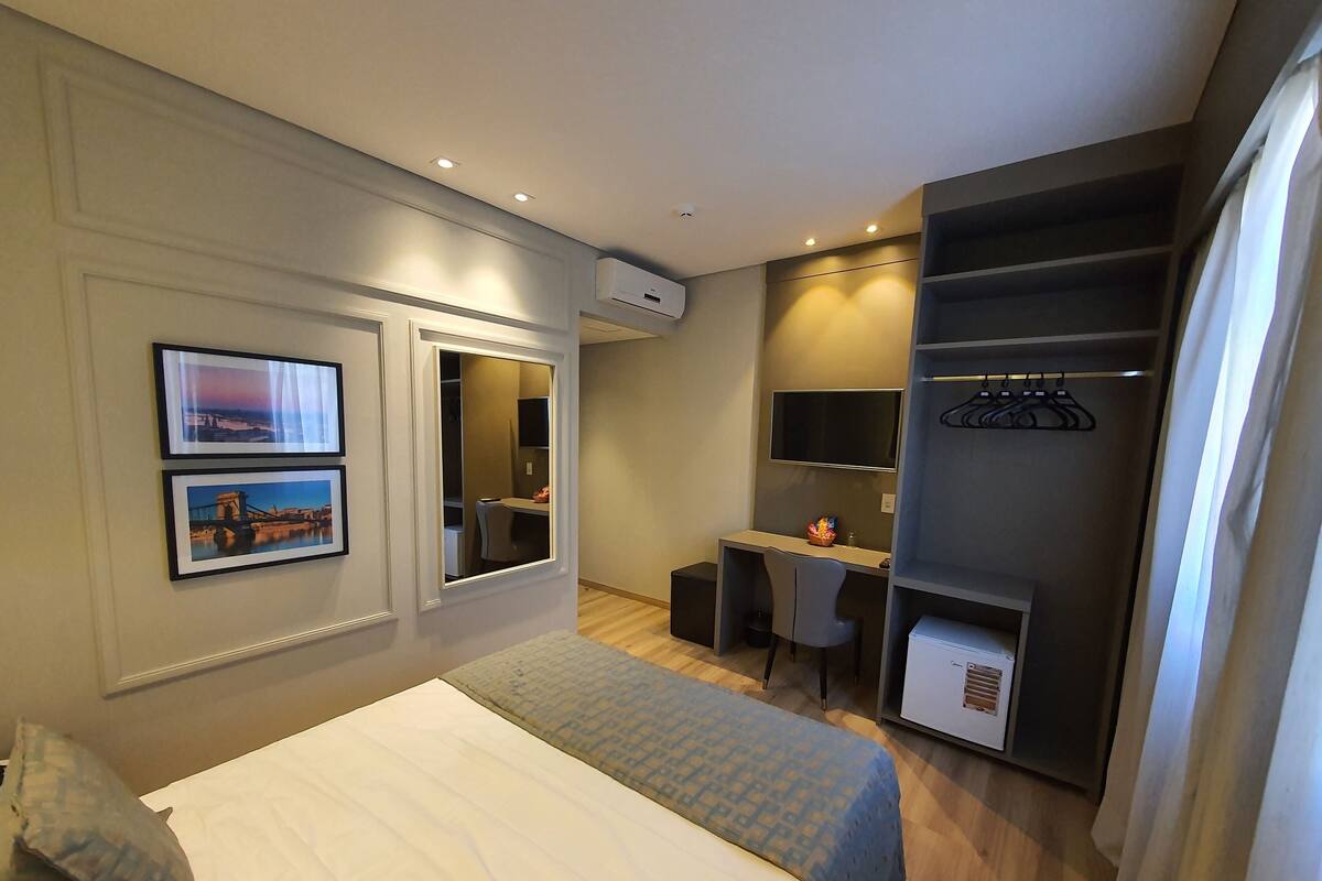Habitación de hotel con cama, escritorio, silla, armario y televisión.