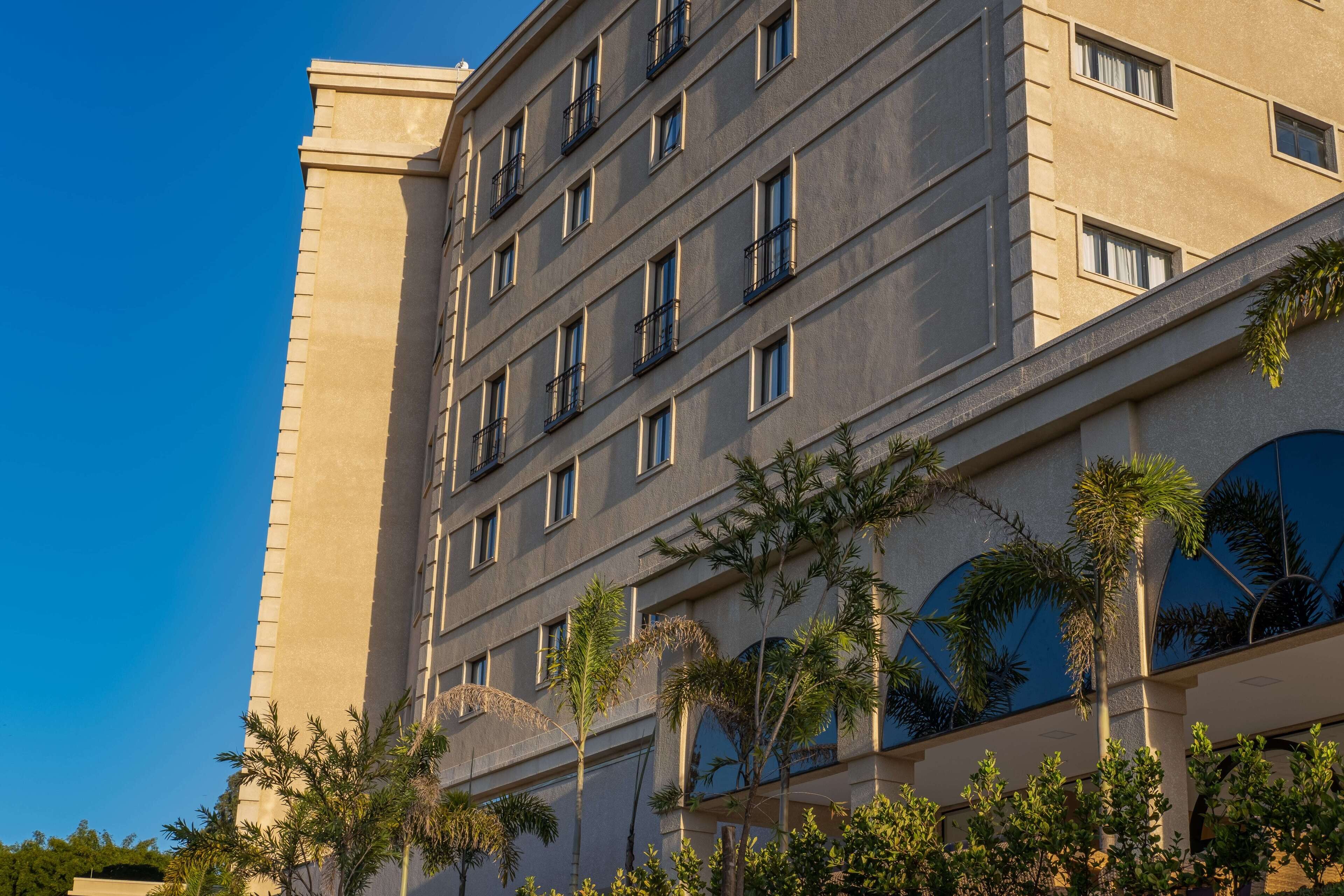 A multi-story hotel with a modern facade, balconies, and palm trees in the foreground.