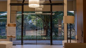A lobby with a glass door leading to a garden, a chandelier, and a sign with information. - Class Hotel Piracicaba (Piracicaba)