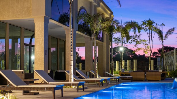 A modern hotel with a pool, lounge chairs, and palm trees. - Class Hotel Piracicaba (Piracicaba)