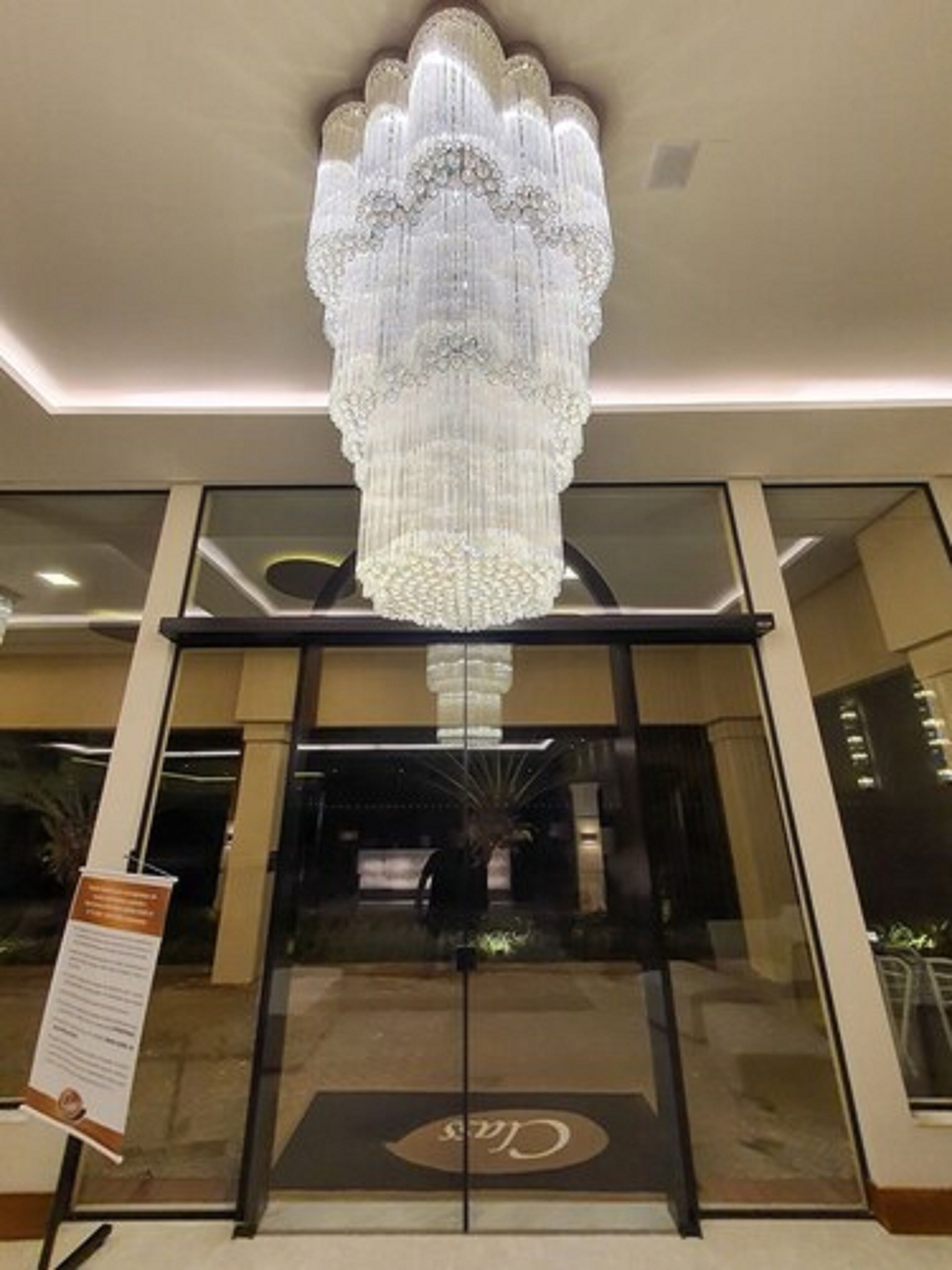 Uma entrada imponente com um lustre grande e ornamentado, e uma porta de vidro com um logotipo.
