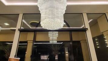 Uma entrada imponente com um lustre grande e ornamentado, e uma porta de vidro com um logotipo.