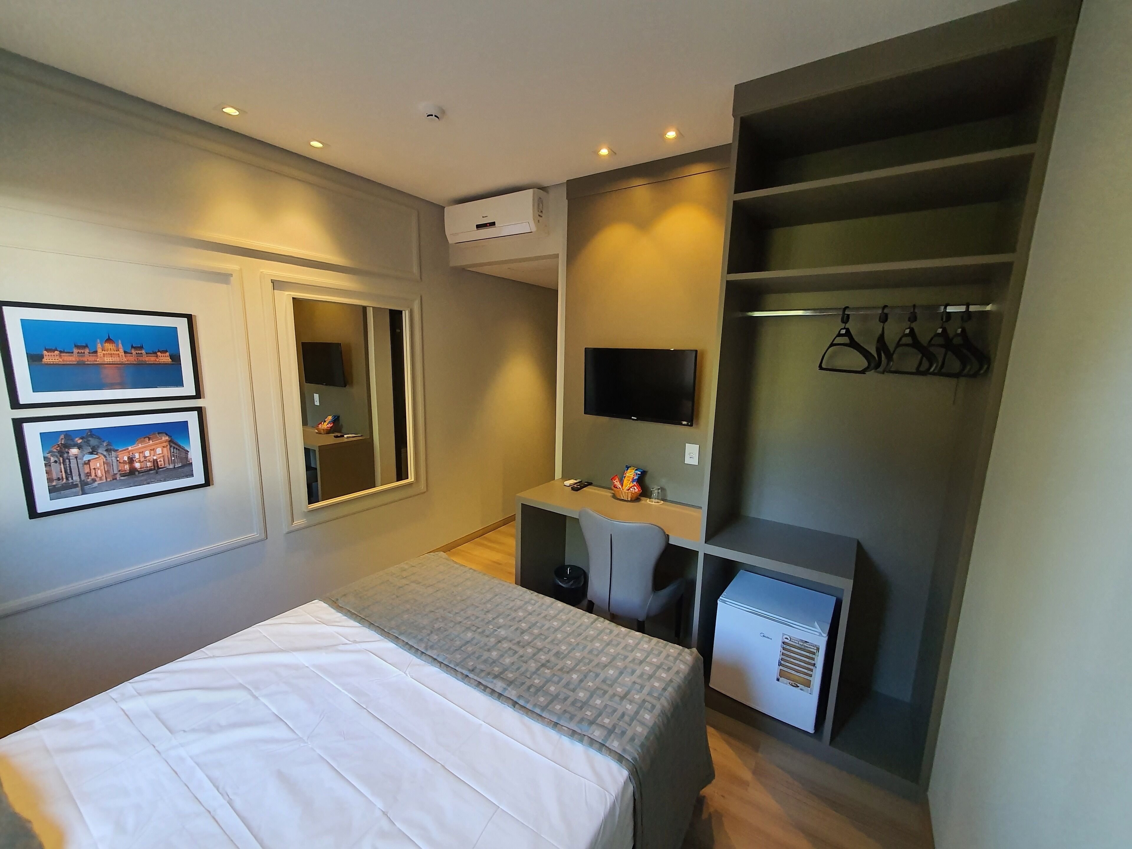 Habitación de hotel con cama, escritorio, silla, televisor, armario y dos cuadros en la pared.