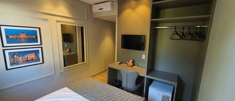 Habitación de hotel con cama, escritorio, silla, televisor, armario y dos cuadros en la pared.