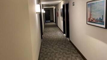 Un pasillo de hotel con piso alfombrado, puertas y un cuadro en la pared.