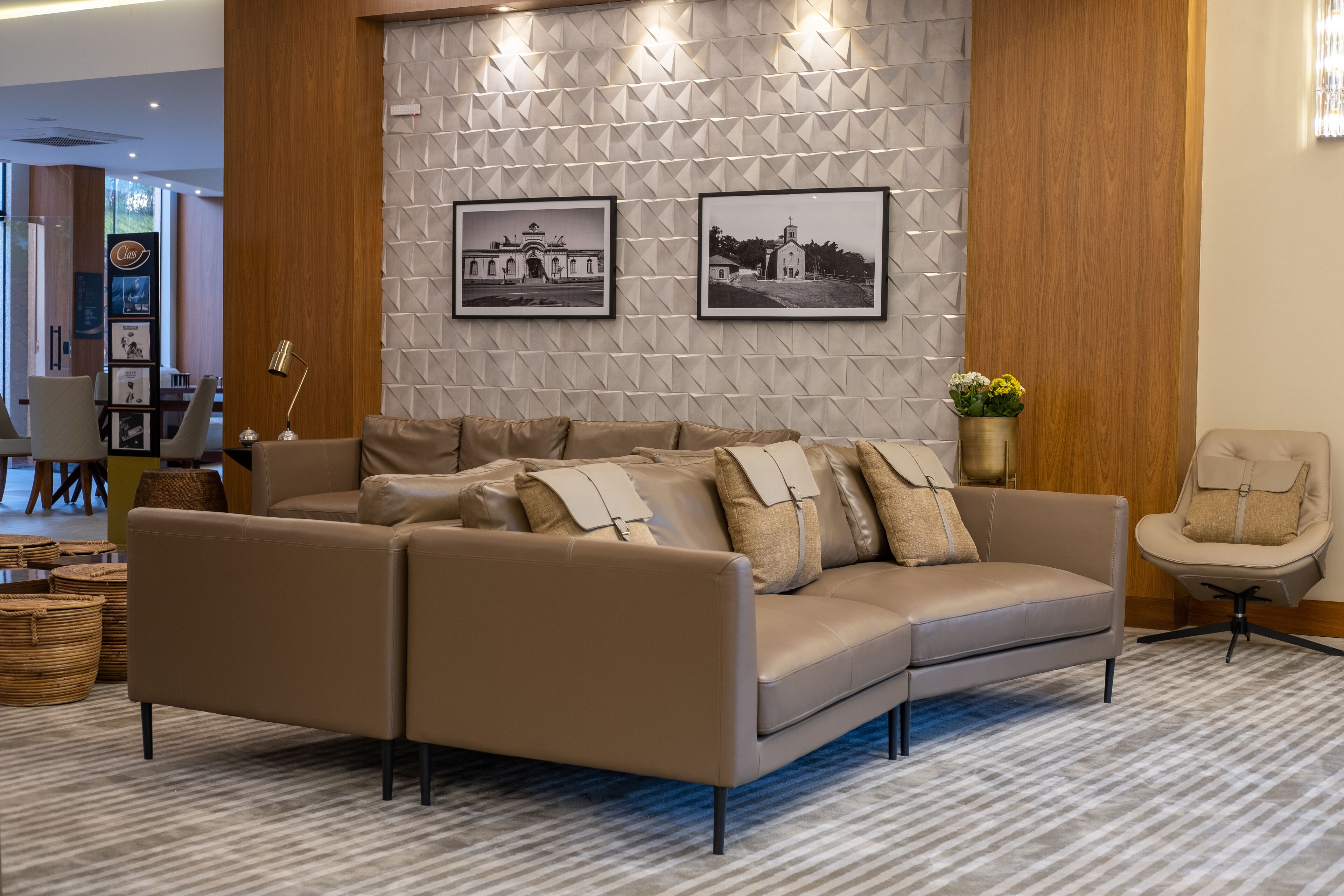 A modern living room with a beige sectional sofa, a wooden accent wall, and two framed black and white photographs.