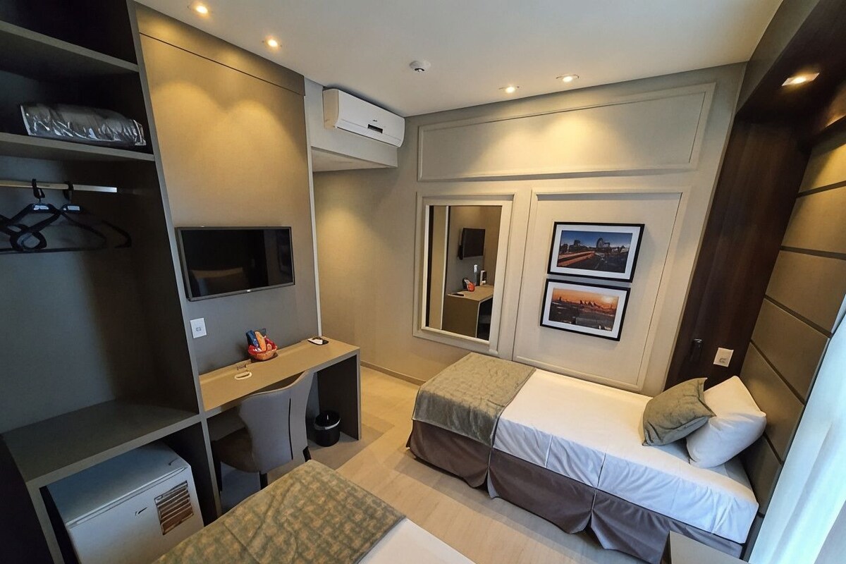 A compact hotel room with a bed, a desk, a chair, a wardrobe, and a television.