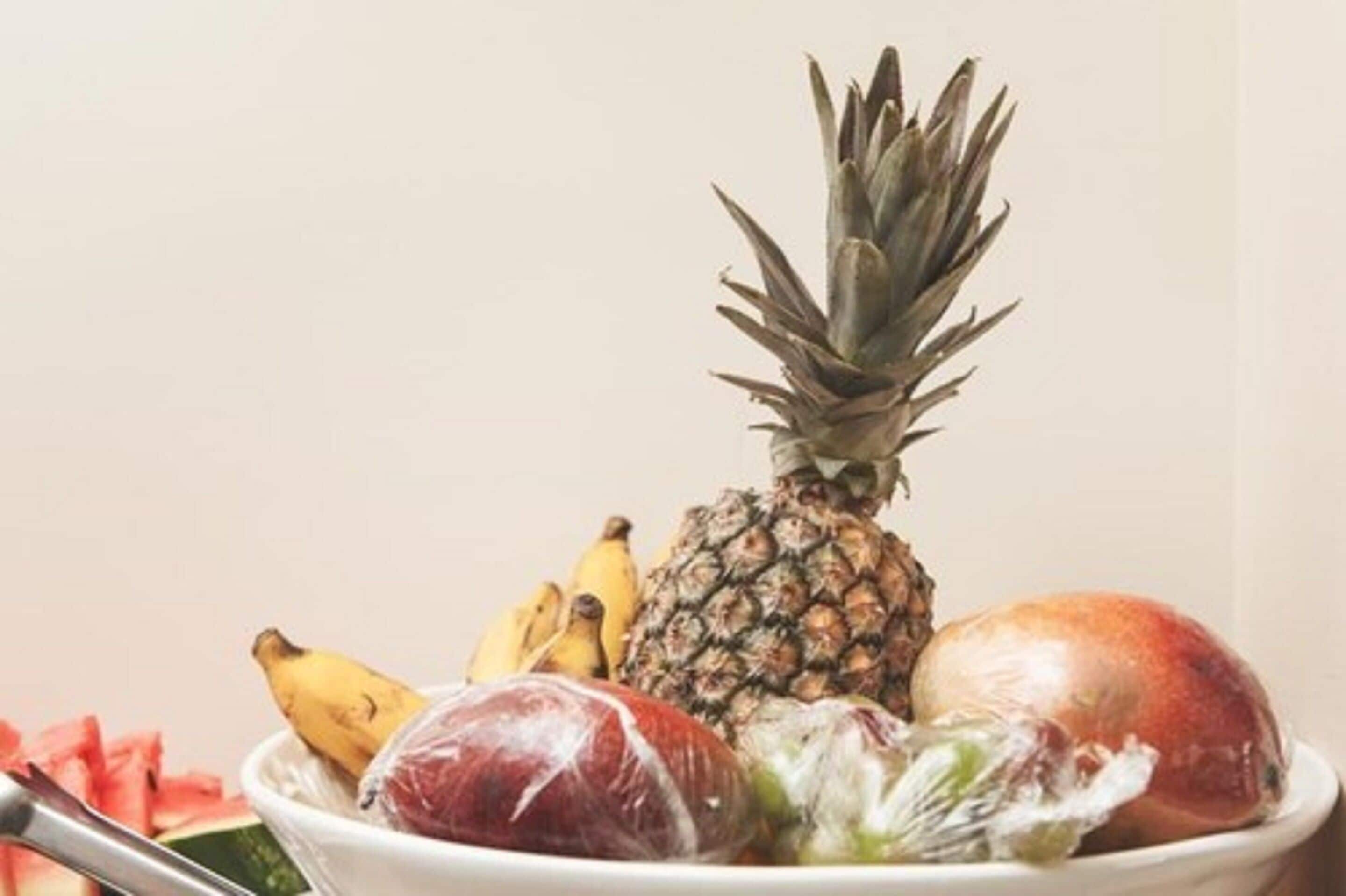 A bowl containing a pineapple, bananas, a mango, and a wrapped fruit.