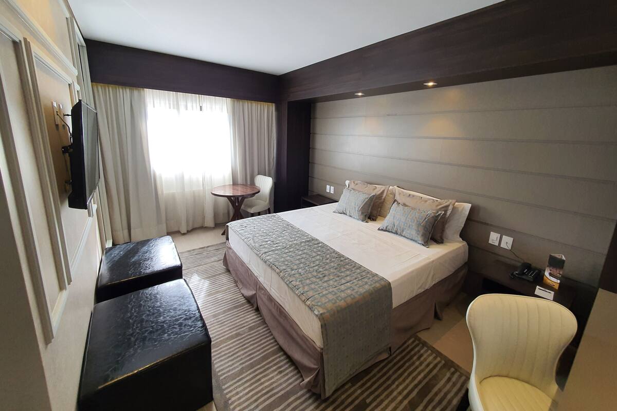 Una habitación de hotel moderna con una cama grande, una mesita de noche, una silla y un televisor montado en la pared.