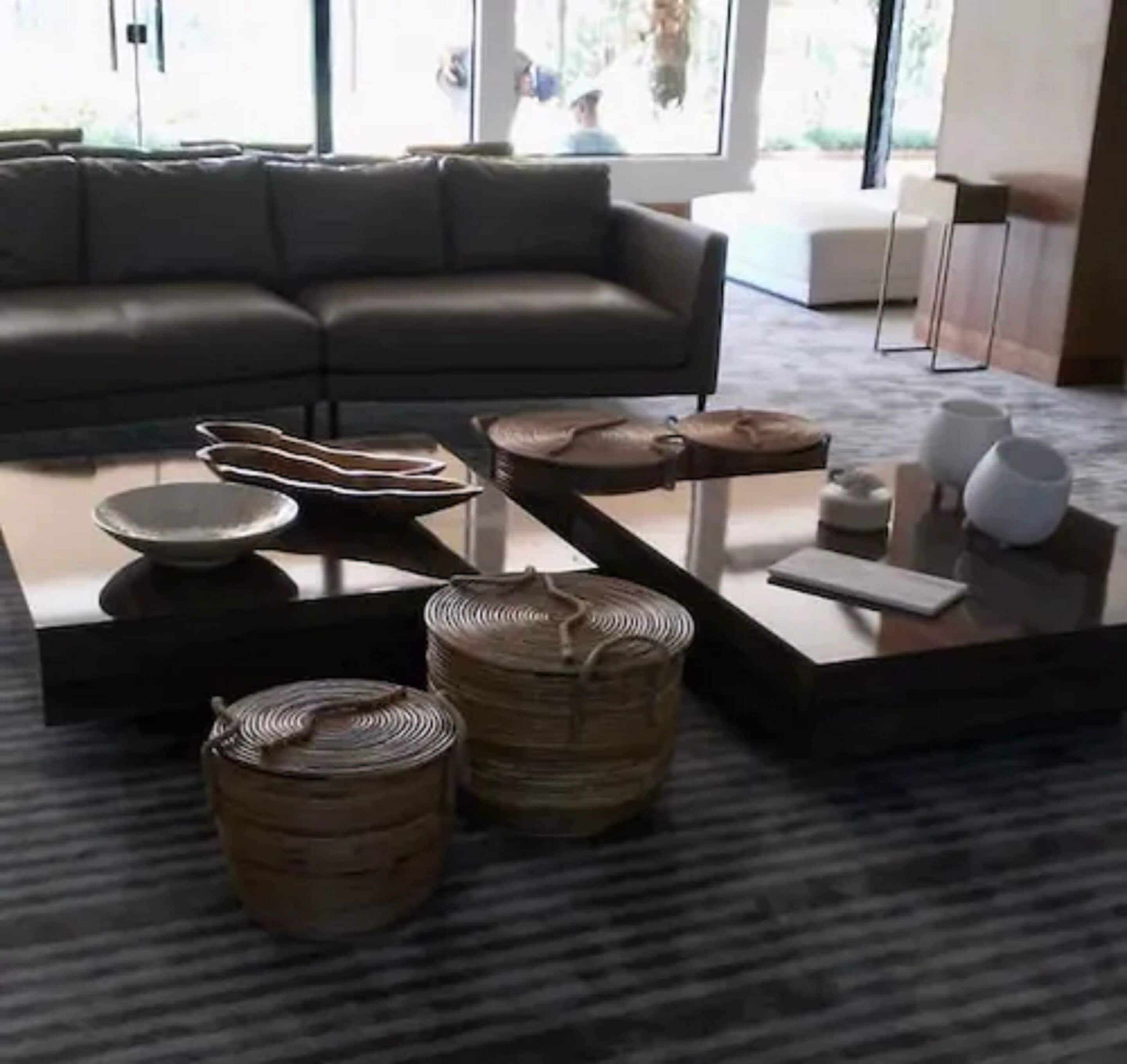 A modern living room with a grey sofa, a coffee table with decorative items, and a view of the outdoors.