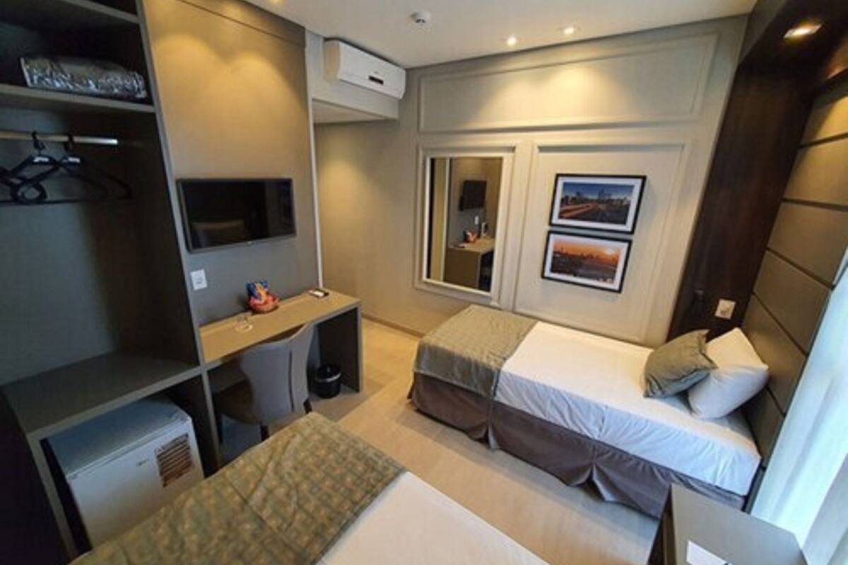 Habitación de hotel pequeña con cama, escritorio, silla, armario y televisor.