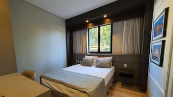 A bedroom with a bed, a desk, and a window with curtains.