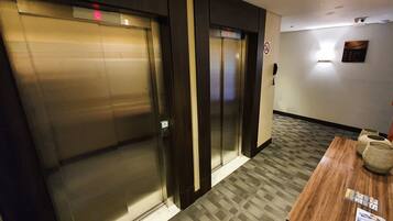 An elevator area with closed doors, a wooden table with a basket, and a wall-mounted sign.