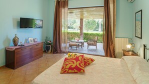 Un dormitorio con cama, televisor, escritorio y vistas a un jardín a través de un ventanal corredero.