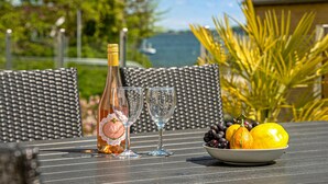 Ein Tisch mit einer Flasche Roséwein, zwei Weingläsern und einer Obstschale mit Trauben, einer Kürbis und einer Zitrone.