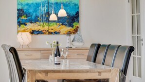 Ein Essbereich mit Holztisch, Ledersesseln, einem Gemälde und Pendelleuchten.