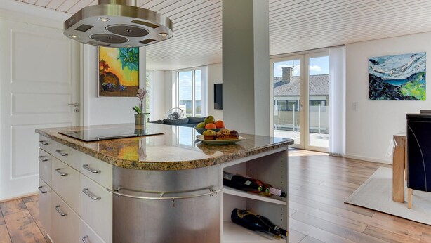 Eine moderne Küche mit einer Granit Arbeitsplatte, Edelstahl Schränken und einem integrierten Weinkühlschrank.
