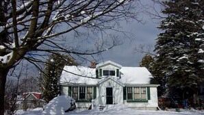 A snow-covered house with a front porch, a chimney, and a small front yard. - Family and Friends 4 Bedroom Newer Vacation Home (Petoskey)
