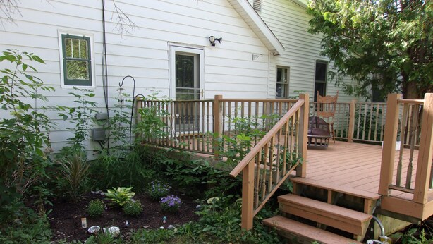 A wooden deck with steps leading to a porch, surrounded by a garden with various plants and flowers. - Family and Friends 4 Bedroom Newer Vacation Home (Petoskey)