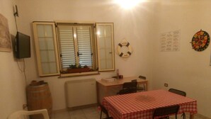 A small dining area with a table covered by a red and white checkered tablecloth, two chairs, a wooden cabinet, a radiator, and a window with blinds. - Self-catering single room for rent with a private bathroom (Marina di Montenero di Bisaccia)