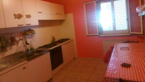 A compact kitchen with white cabinets, a gas stove, and a window with blinds. - Self-catering single room for rent with a private bathroom (Marina di Montenero di Bisaccia)