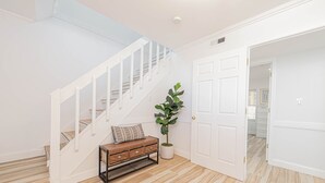 Una escalera con barandillas blancas, un banco de madera con cajones y una planta en maceta.