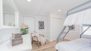 Un dormitorio con una cama individual superpuesta, una mesita de noche con adornos, una silla con una manta y una pared decorada con motivos artísticos.