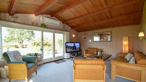 A cozy living room with a television, wicker furniture, and a view of the outdoors. - Beach front home in Stubbekøbing (Stubbekøbing)