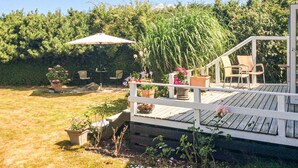 A wooden deck with outdoor seating, surrounded by a garden with various plants and flowers. - Beach front home in Stubbekøbing (Stubbekøbing)