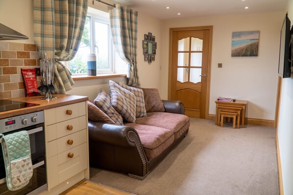 A cozy kitchen with a brown leather sofa, a wooden cabinet, and a window with plaid curtains.